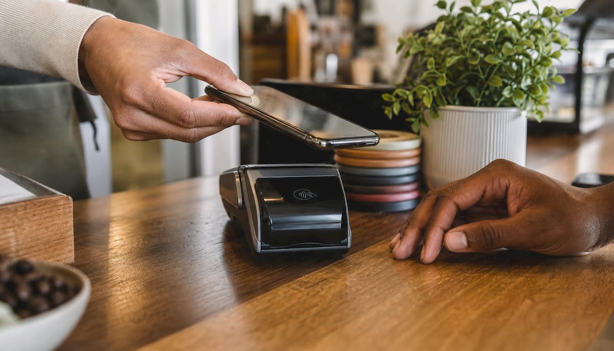 Hands holding phone near payment reader for NFC transaction