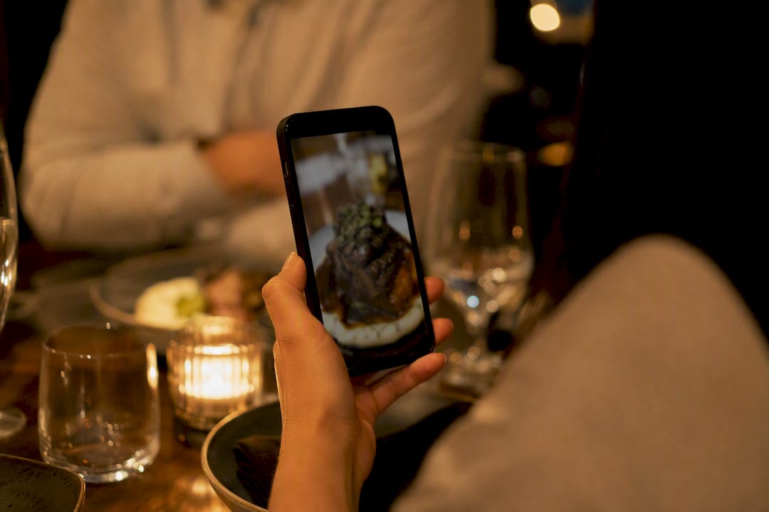 Hand holding phone with guest food photo in restaurant