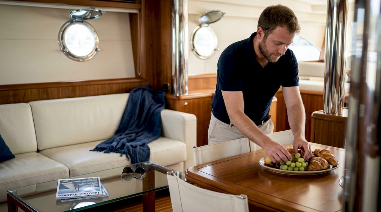 Lo steward dello yacht si occupa di allestire un elegante aperitivo nel raffinato salone, curando ogni dettaglio per offrire agli ospiti un momento di puro piacere.