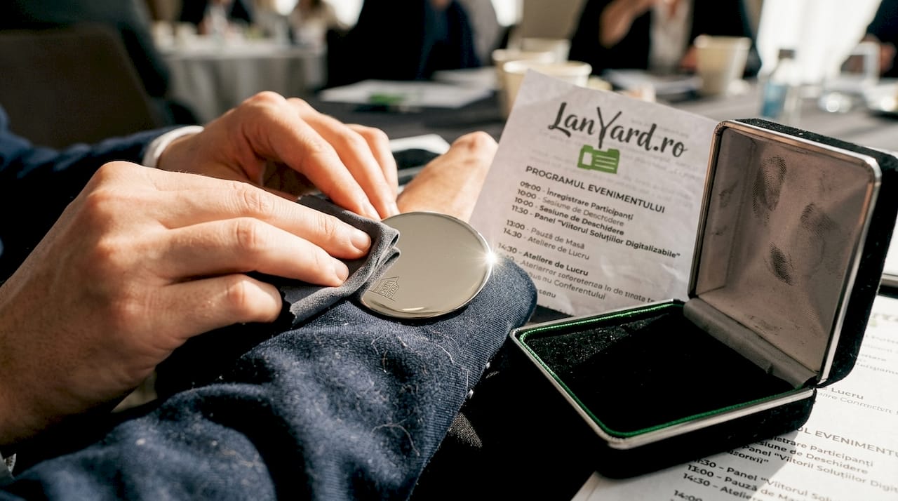 Două mâini lustruiesc cu grijă o insignă metalică pentru un eveniment, pentru ca aceasta să arate impecabil.
