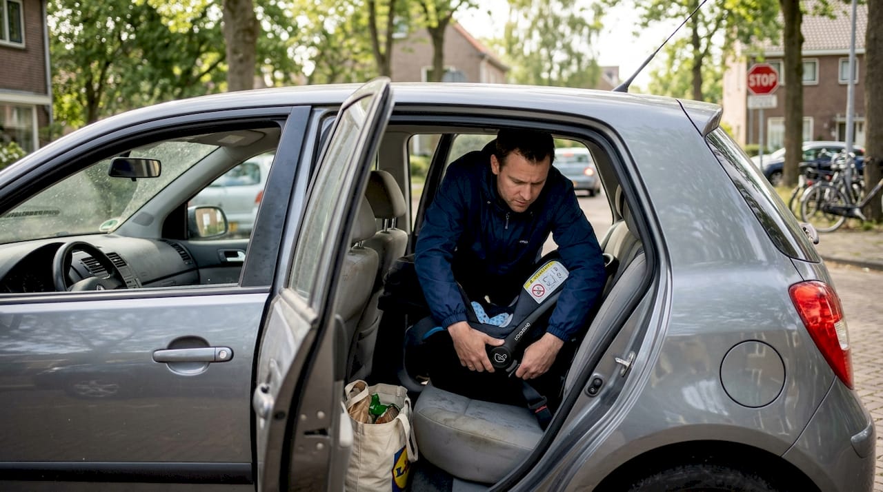 Vader kijkt of het autostoeltje van de baby goed vastzit