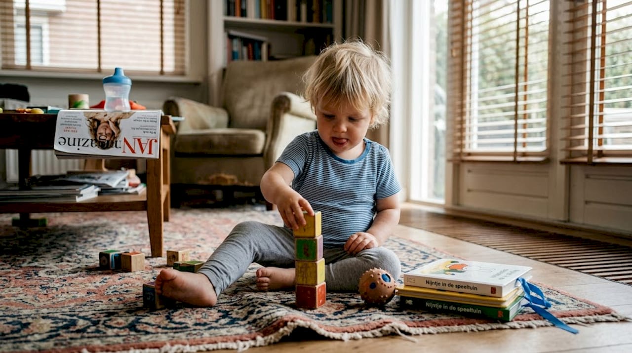 Een peuter zit gezellig op het kleed in de woonkamer en bouwt een toren van blokken.