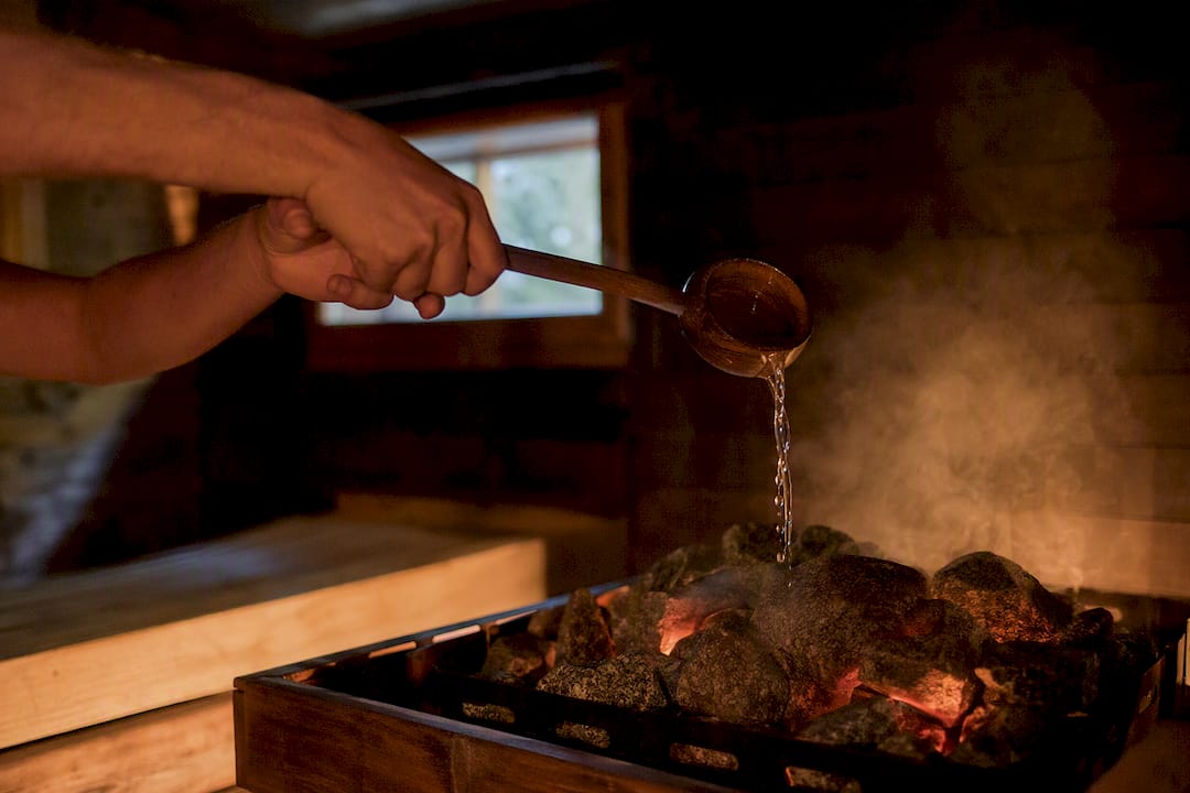 Hands pouring water on hot sauna stones
