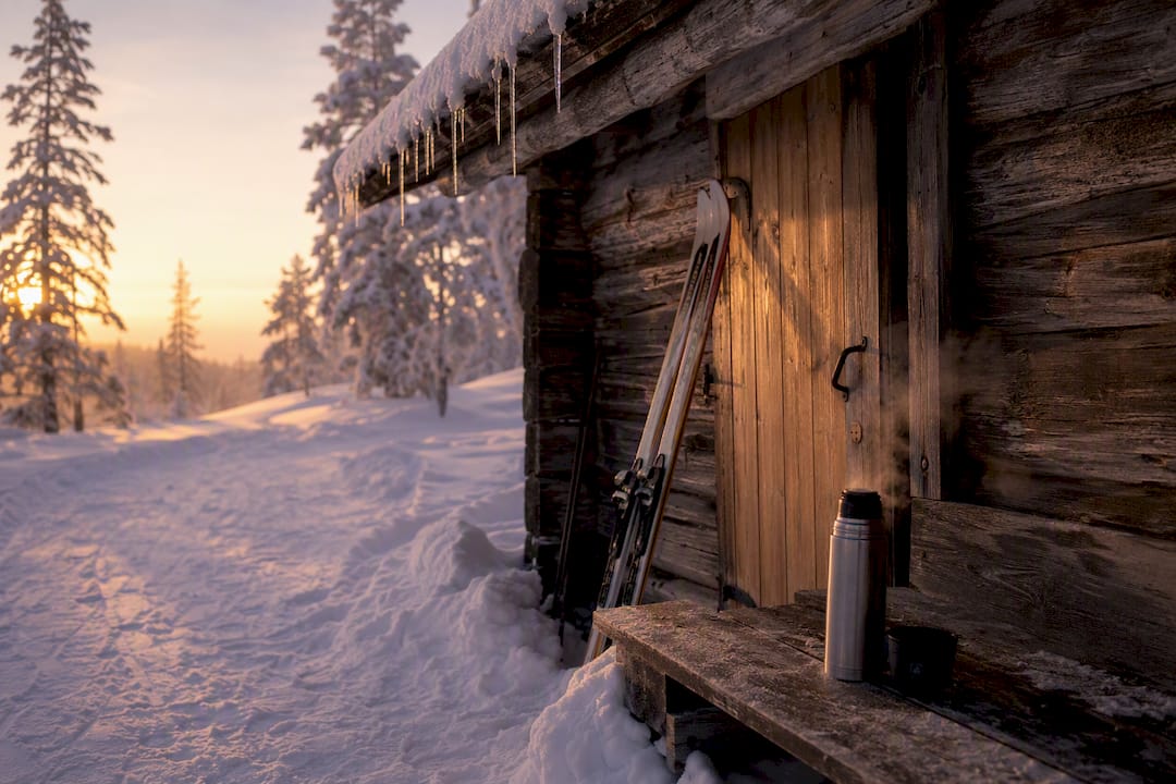 Snow-covered rustic ski hut with skis outside