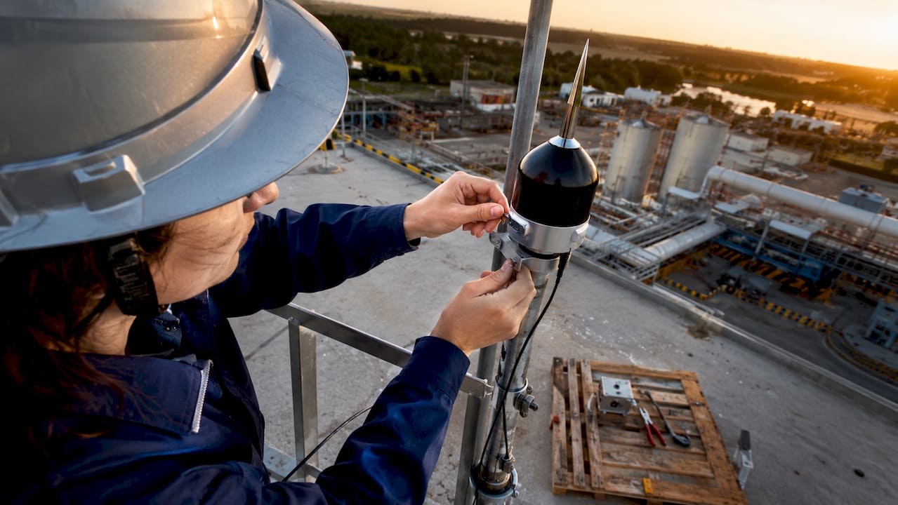 Mains d’une technicienne en pleine installation d’un capteur de paratonnerre sur un site classé ATEX.