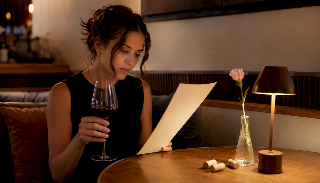 Hands holding wine list and wine glass over table