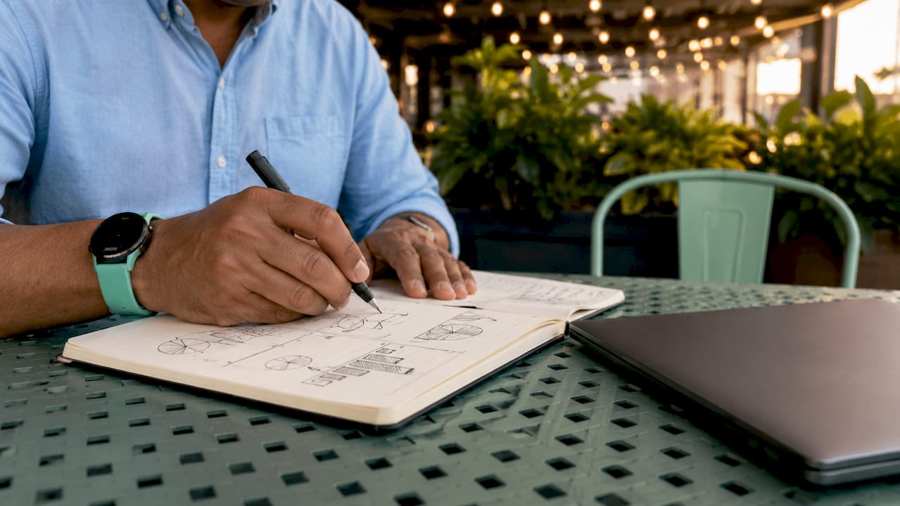Personas tomando apuntes en un cuaderno mientras trabajan en un espacio compartido