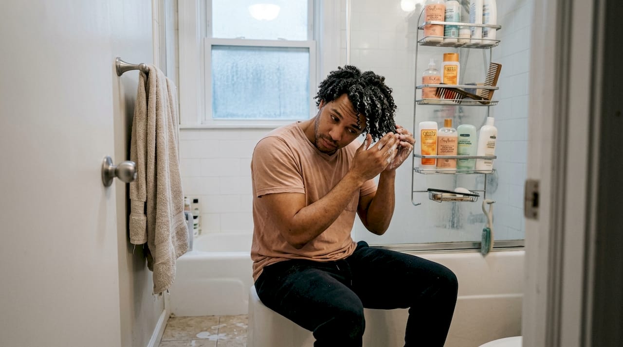 Man conditioning curly hair in home bathroom