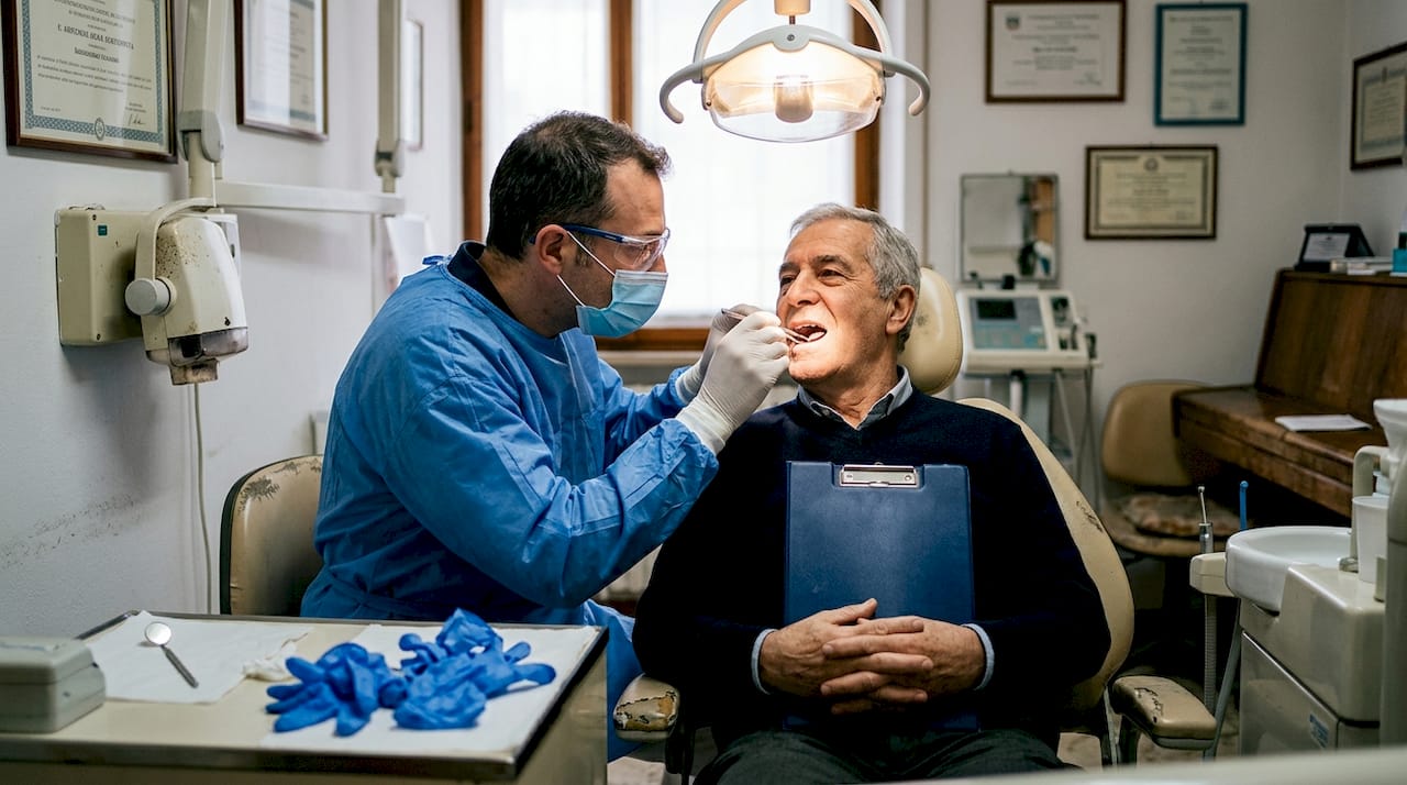 Il dentista esegue un controllo alle gengive di un paziente anziano.