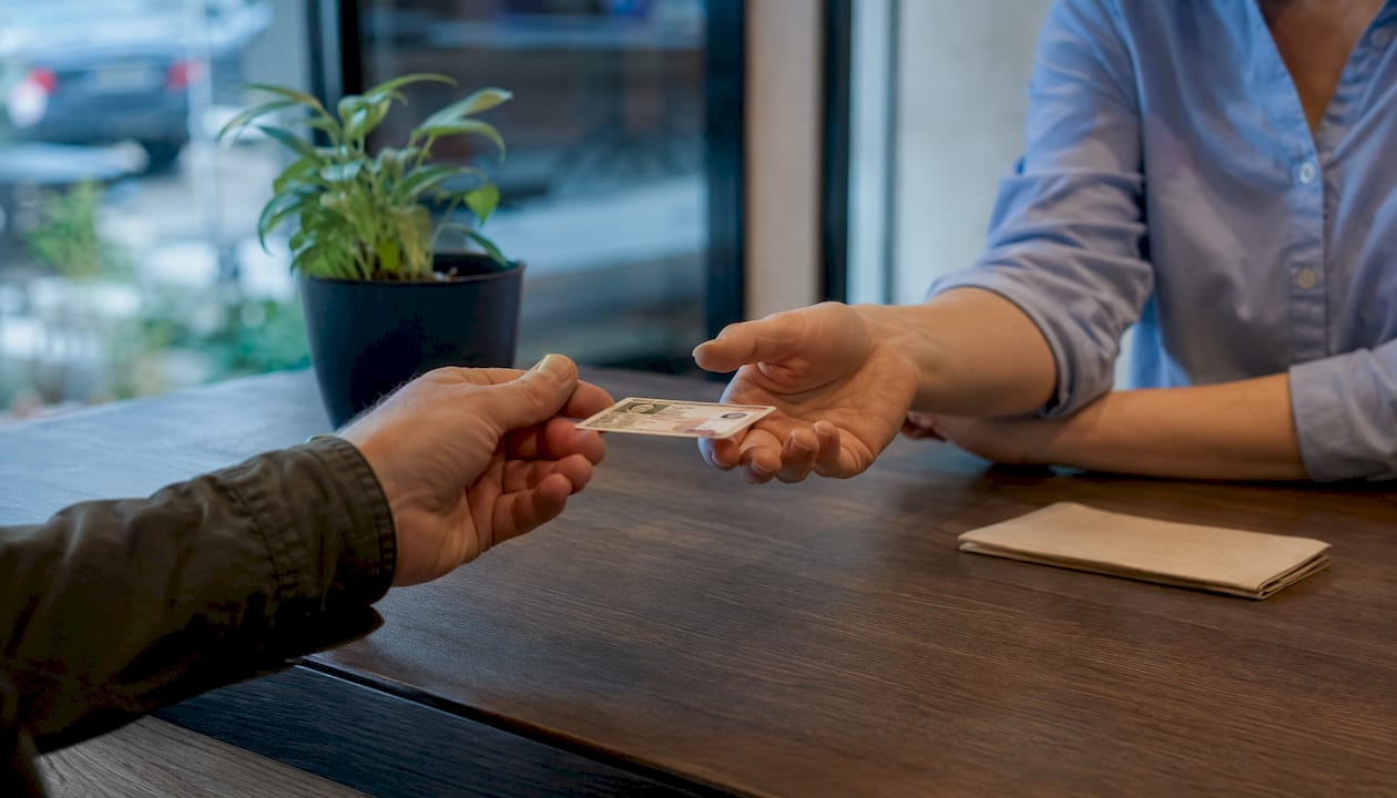 Prie banko langelio klientas perduoda savo asmens dokumentą darbuotojui patikrinimui.