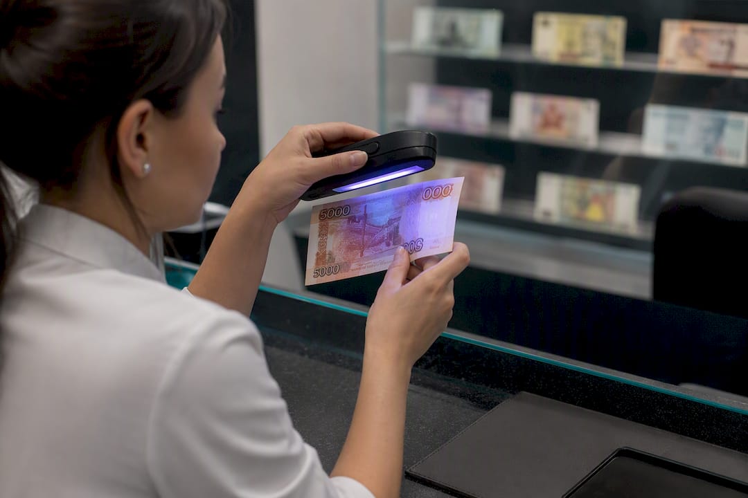 Banko darbuotojas tikrina rublio kupiūrą po ultravioletine lempa, siekdamas įsitikinti jos autentiškumu.