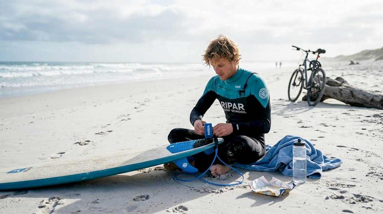 Surfer preparing gear on sandy beach