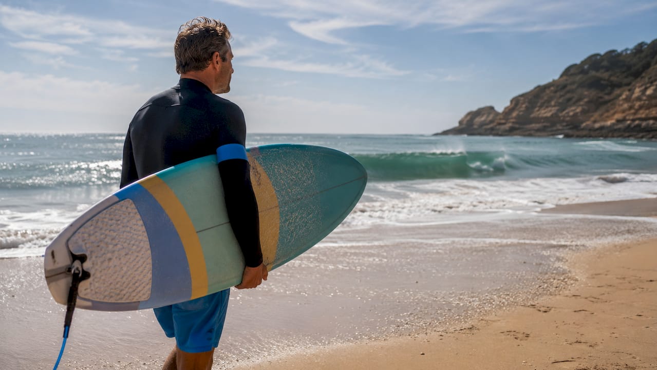Surfer walking on beach with offshore clean waves