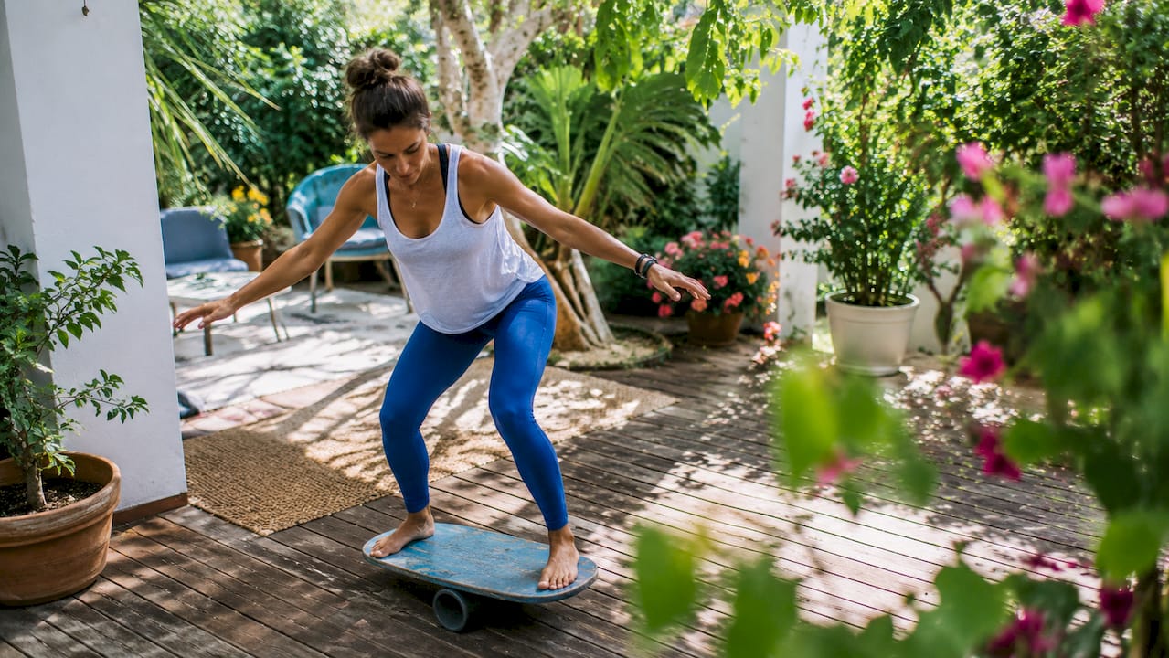 Woman balancing on dryland surf training board in home gym