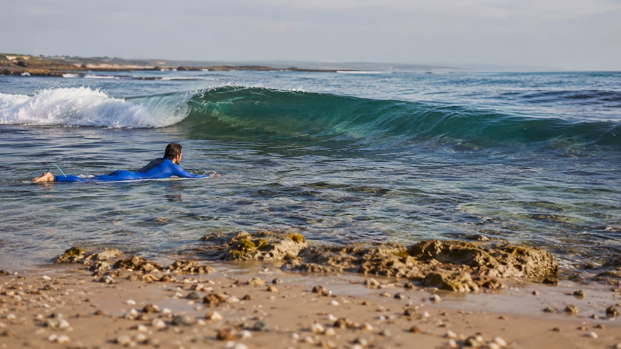 Surfer paddling at reef break during high tide