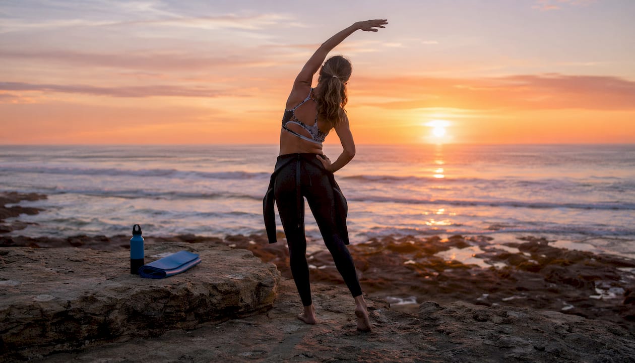 Female surfer stretching on beach at sunrise