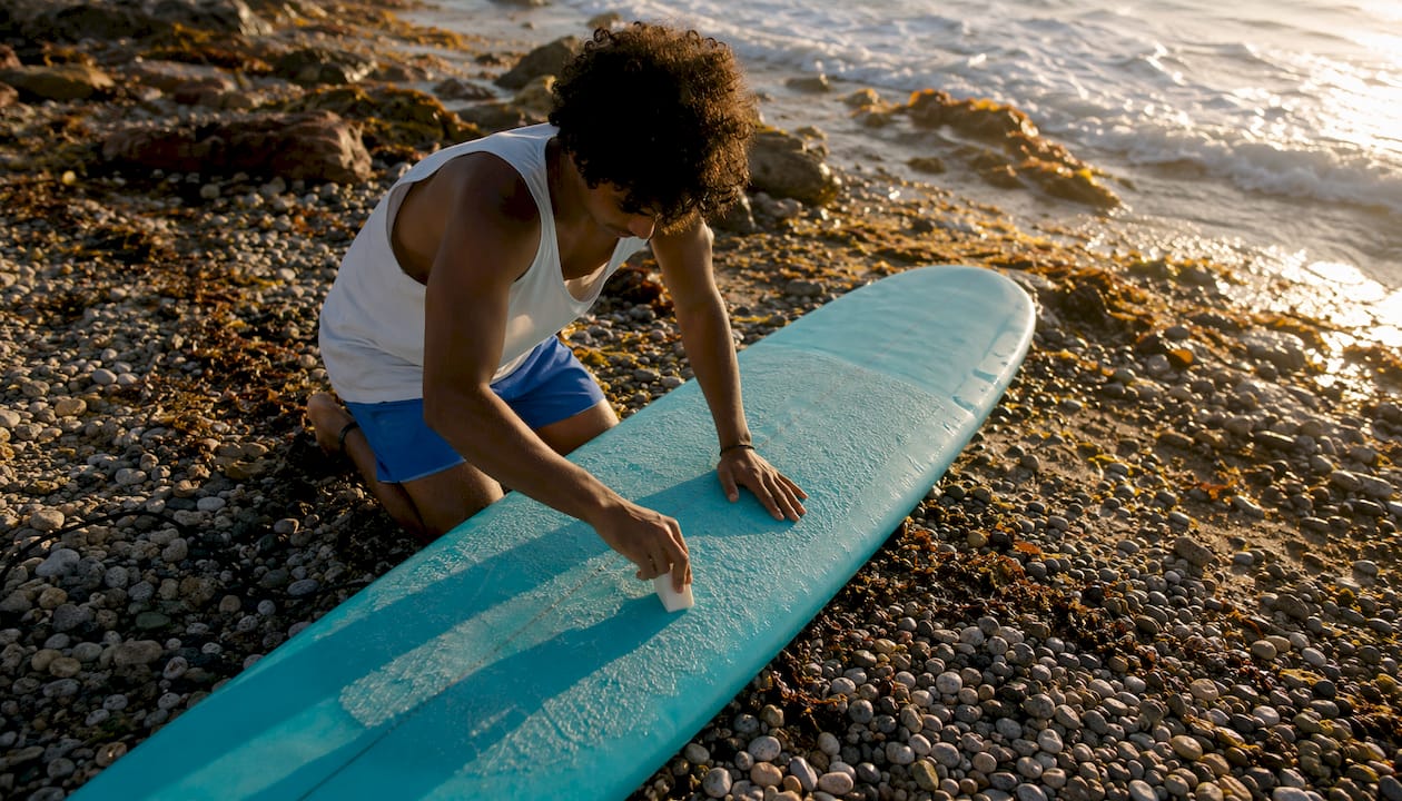 Surfer applying wax to surfboard on beach