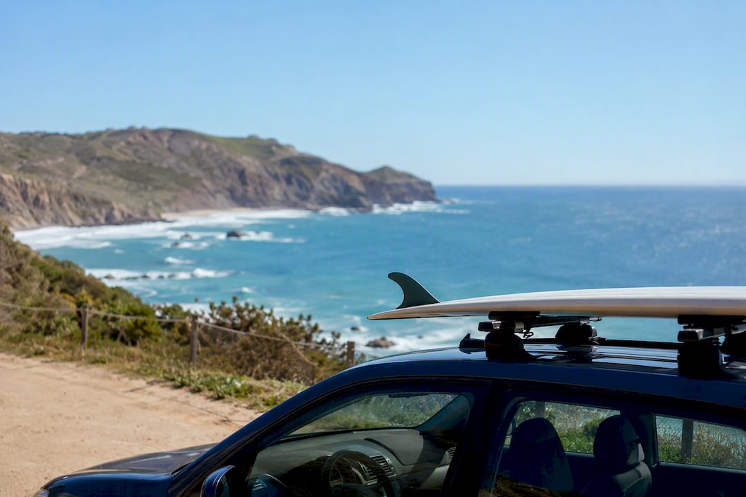 Car with surfboard roof rack on coastal road at sunrise