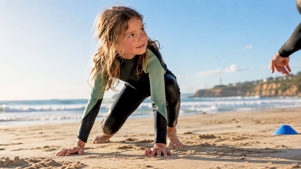 Child practicing a surfing pop-up on sand