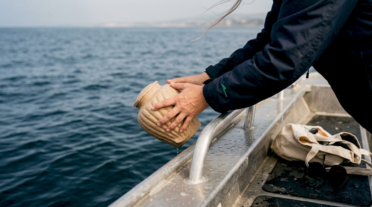 Hands lowering shell urn into ocean