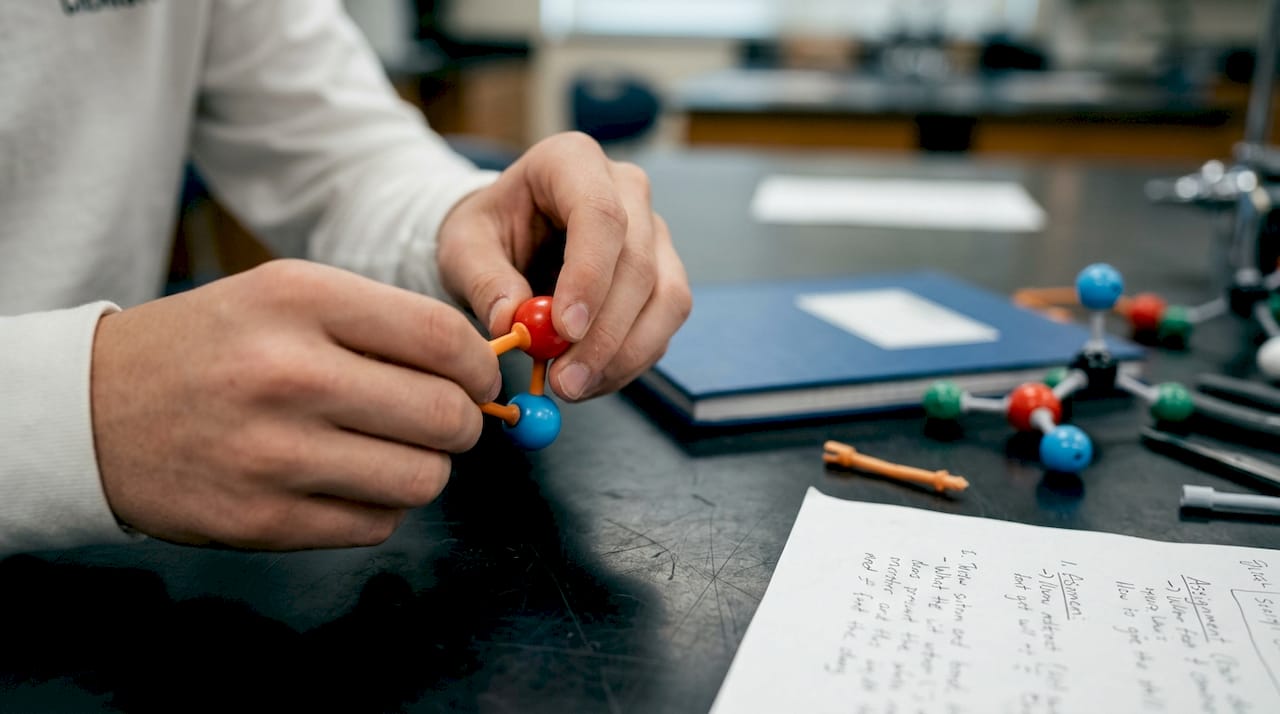 Hands building molecules with model kit