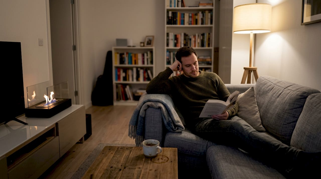 Un homme plongé dans sa lecture, installé confortablement près d’une cheminée au bioéthanol.