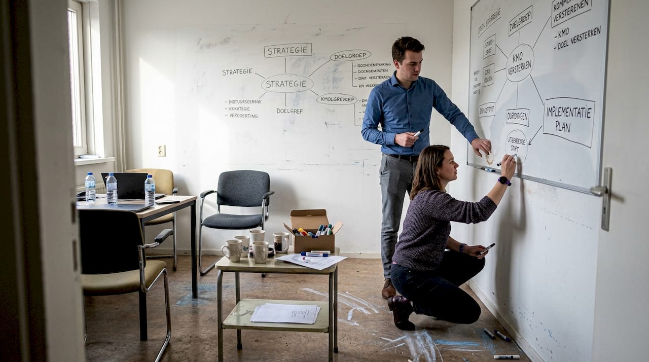Het team verzamelt zich rond het whiteboard om samen ideeën uit te wisselen.
