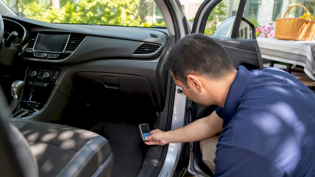 Hand holding testing device near vehicle floor carpet