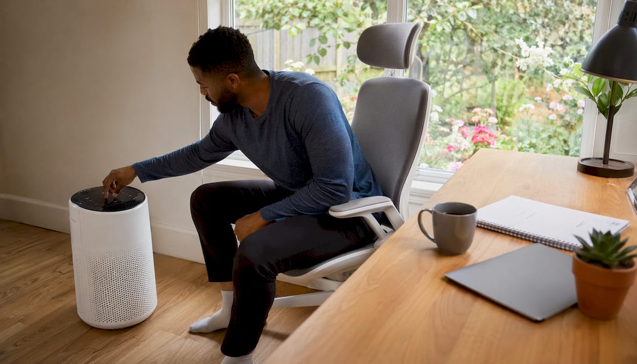 Man adjusting air purifier near open window in living room