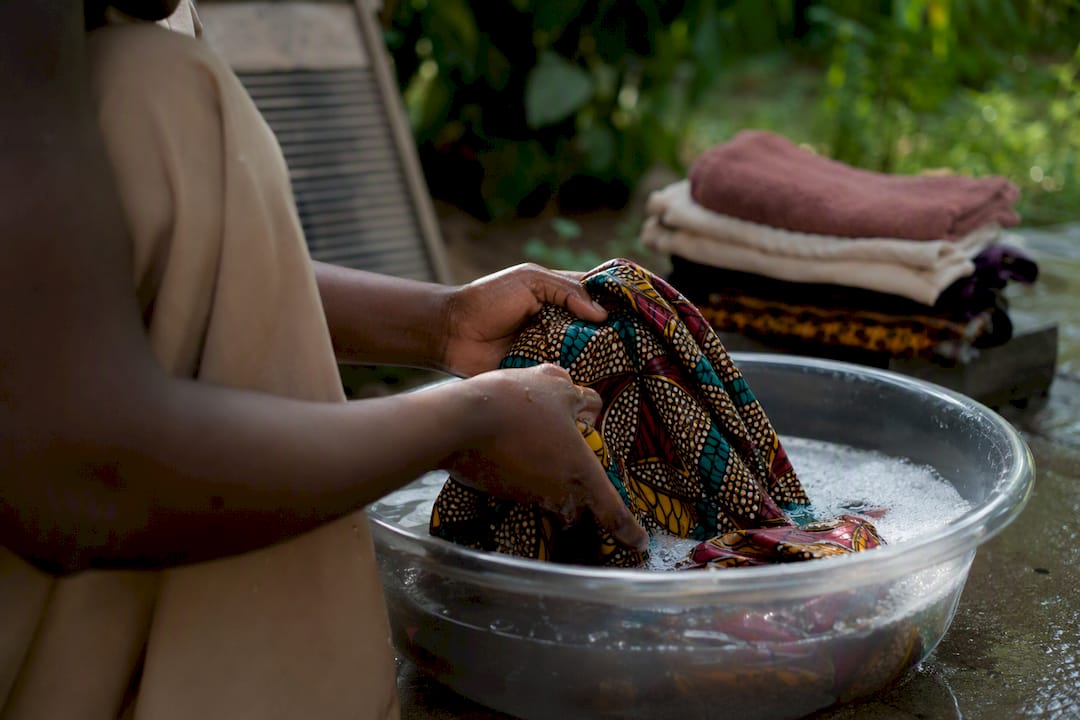Hands gently hand-washing Ankara fabric in water basin