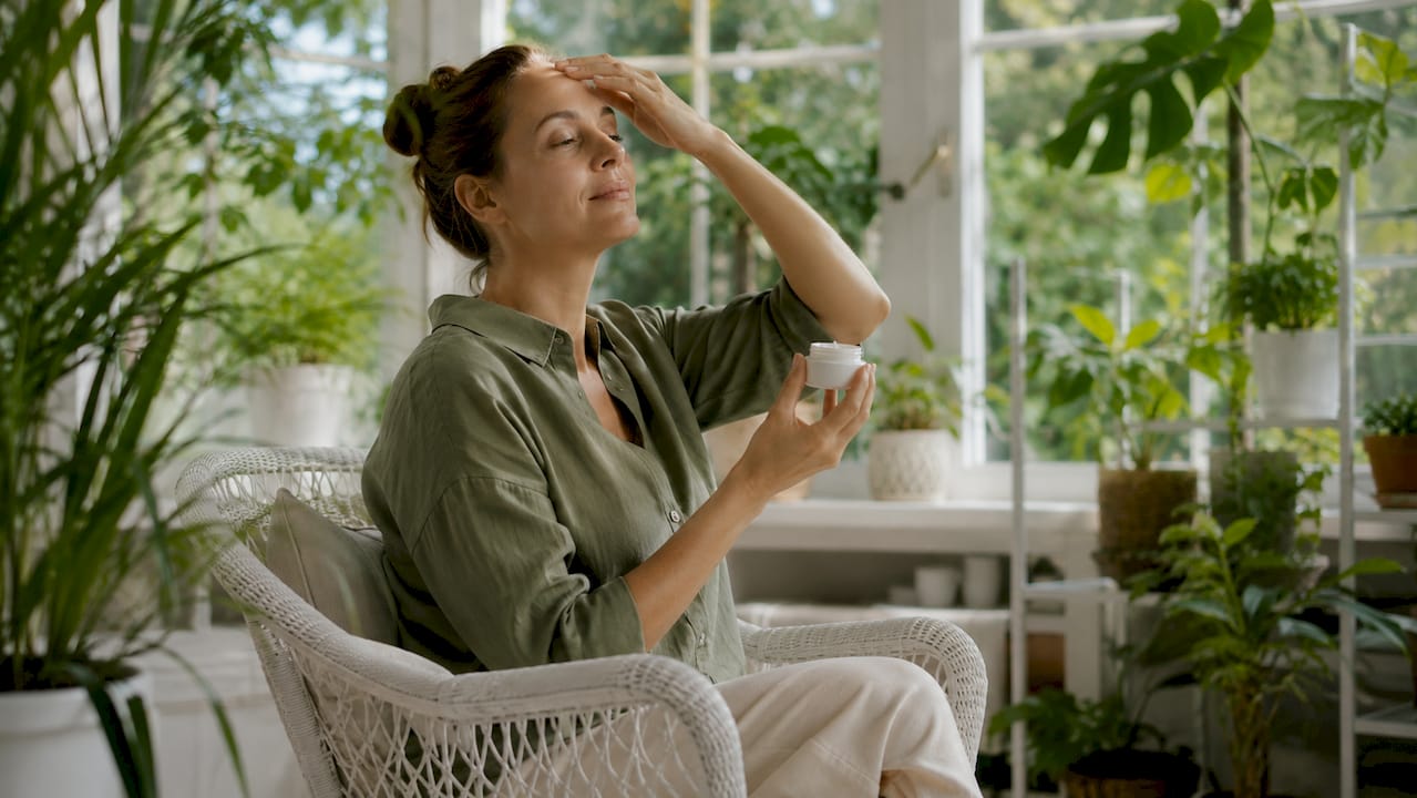 Woman applying moisturizer in garden setting