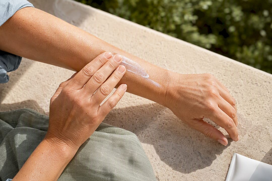 Mature woman applying sunscreen to forearm