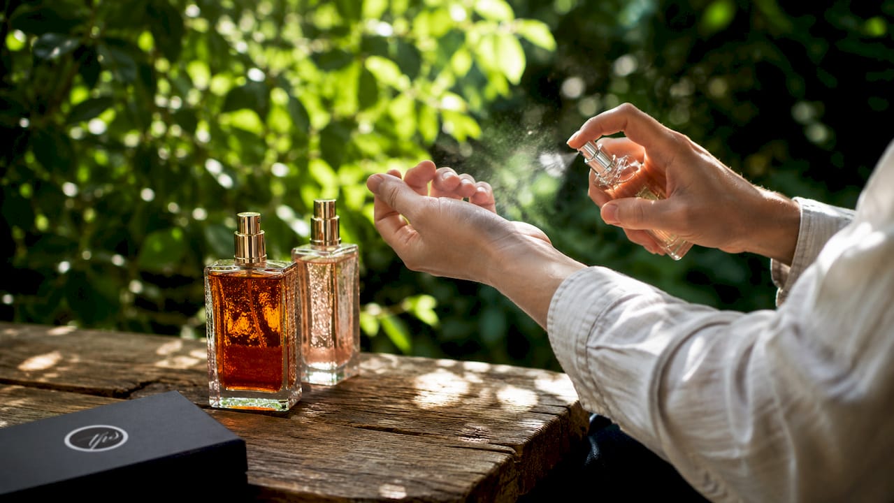 Close-up hands layering perfume sprays on skin