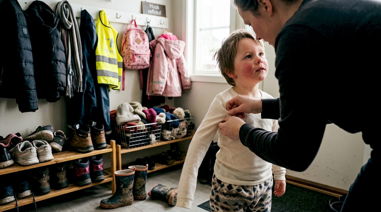 En forelder hjelper barnet sitt med å ta på et lag med myk merinoull.