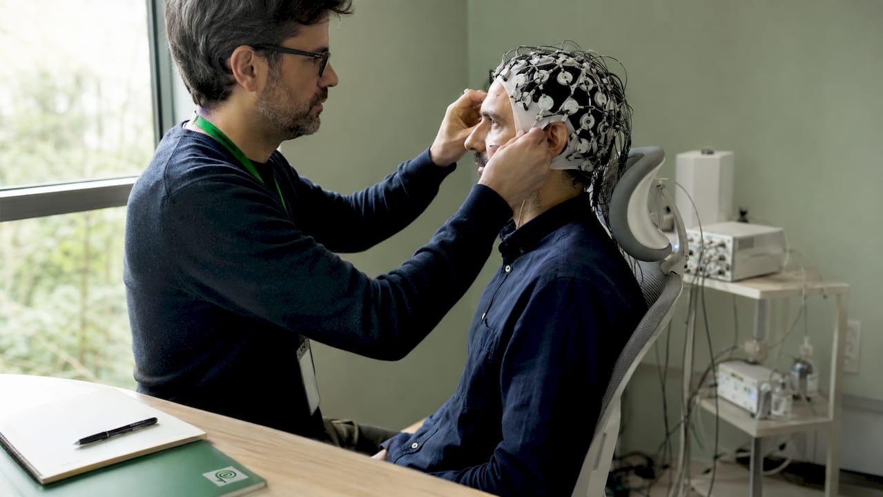 Un operatore sistema con cura il casco per l’elettroencefalogramma sulla testa del paziente.