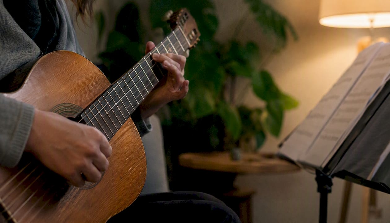 Le mani che si muovono sulle corde della chitarra, immerse nel calore di una stanza accogliente.