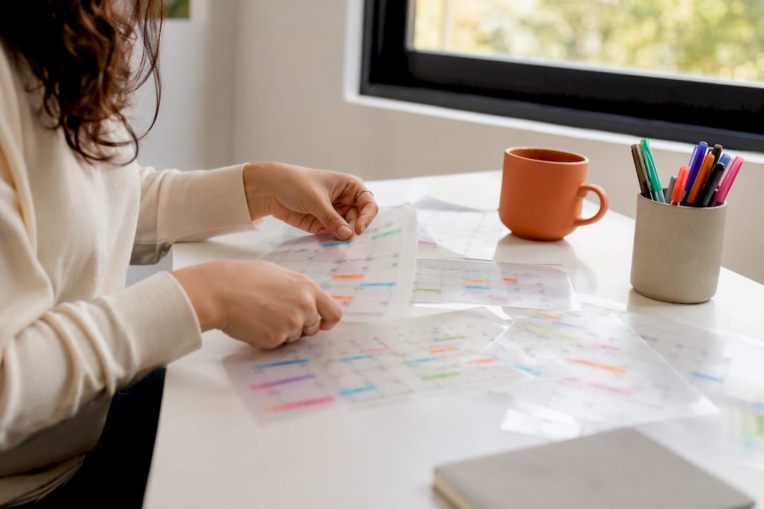 Hands organizing layered calendars on desk