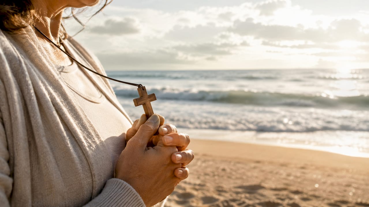 Hands holding wooden cross pendant outdoors