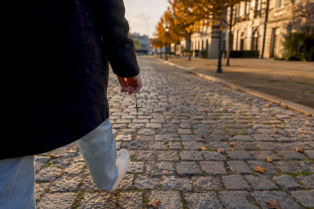 Feet walking on city path holding cross pendant