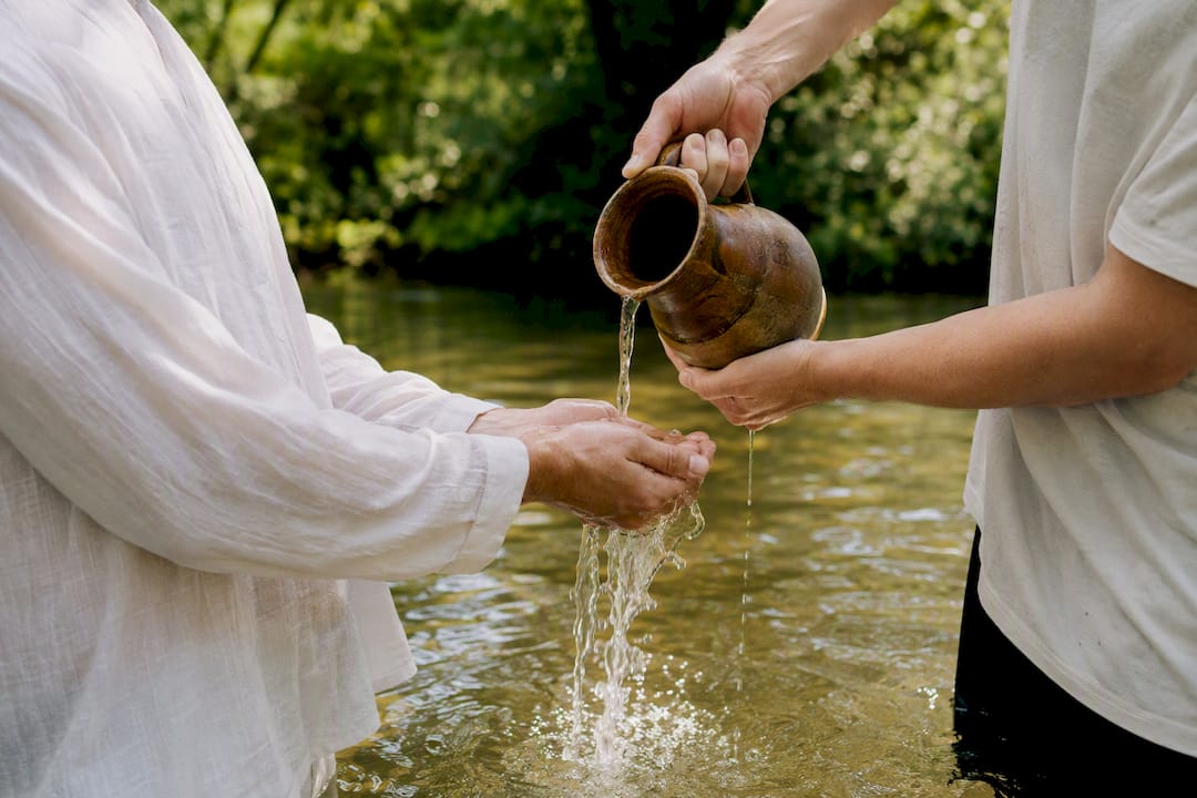 Hands pouring water symbolizing baptism outdoors