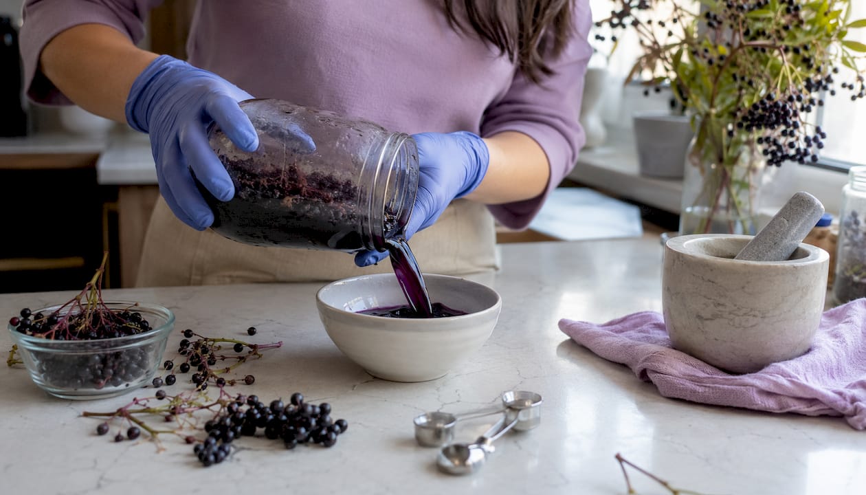 Hands stirring jar of plant pigment maceration for skincare