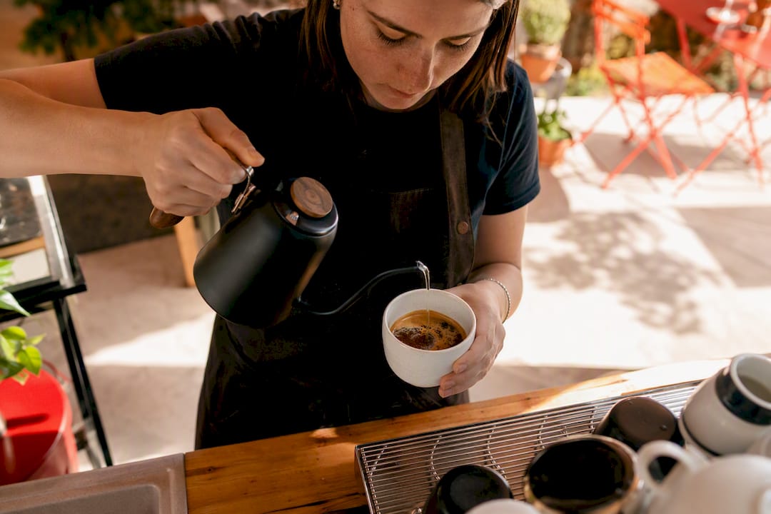 Hands pouring hot water into espresso for Americano