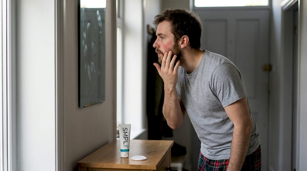 Man checking facial redness in hallway mirror