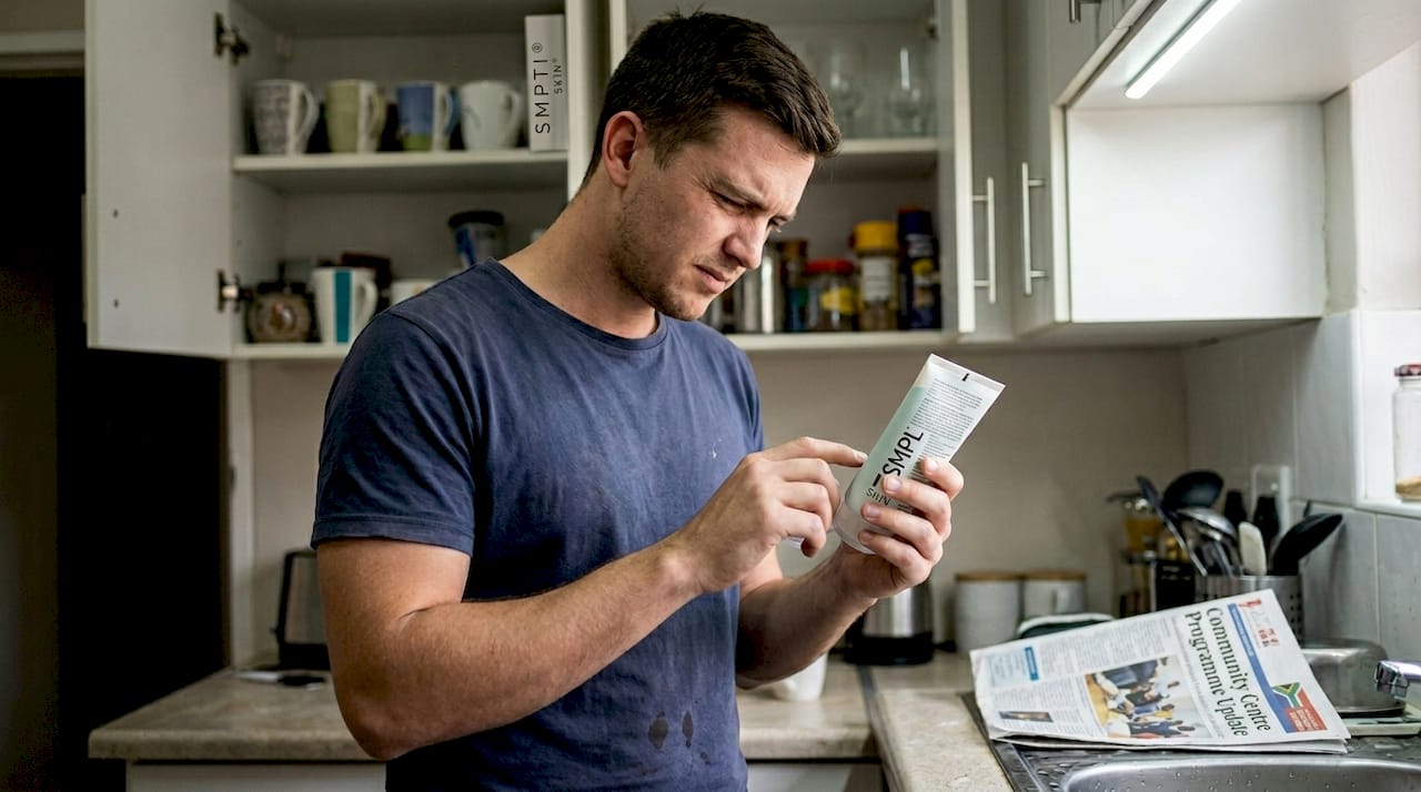 Man reading skincare product label at kitchen