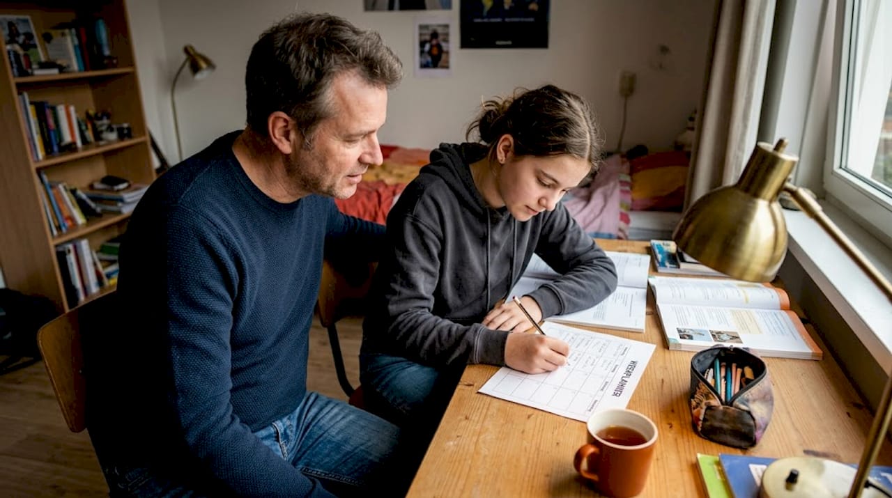 Vader en dochter bespreken samen het huiswerk op haar slaapkamer.