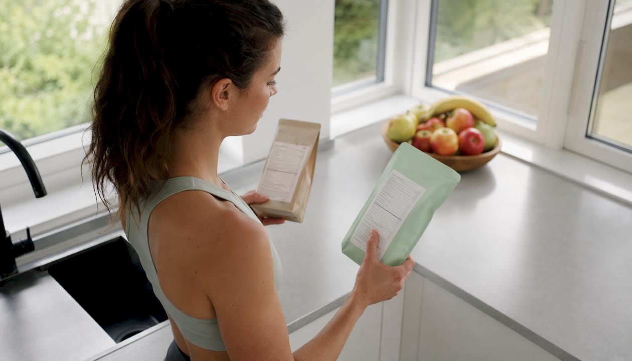 Zwei Hände halten Lebensmittelpackungen nebeneinander und prüfen die Zutatenlisten.