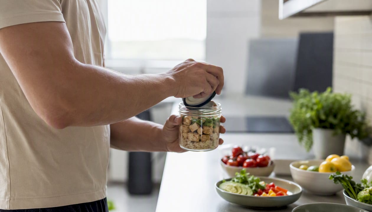 Eine Hand dreht den Deckel eines proteinreichen Gerichts im Glas auf.