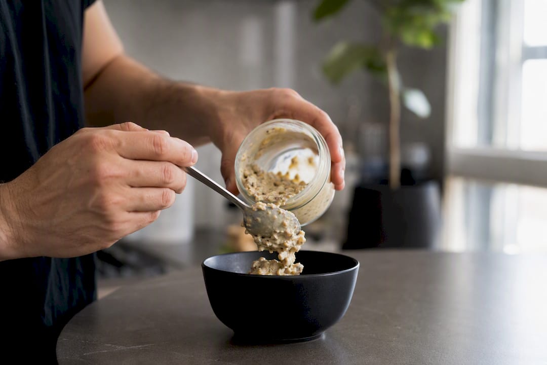 Hände servieren eine proteinreiche Mahlzeit aus dem Glas auf den Teller