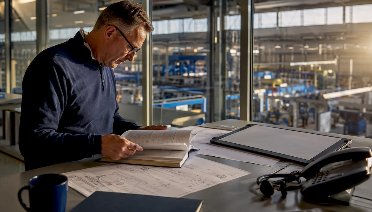 En inköpare sitter vid sitt skrivbord på kontoret och går igenom leverantörsguiden för industrin.