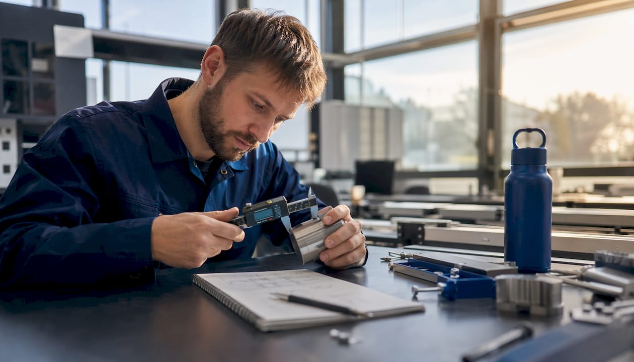 En tekniker kontrollmäter en metallkomponent med hjälp av ett digitalt skjutmått.